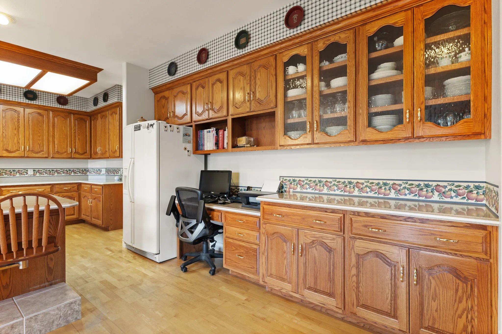 Kitchen area featuring light wood-finish flooring, extensive wood cabinetry, white countertops, and a built-in desk space