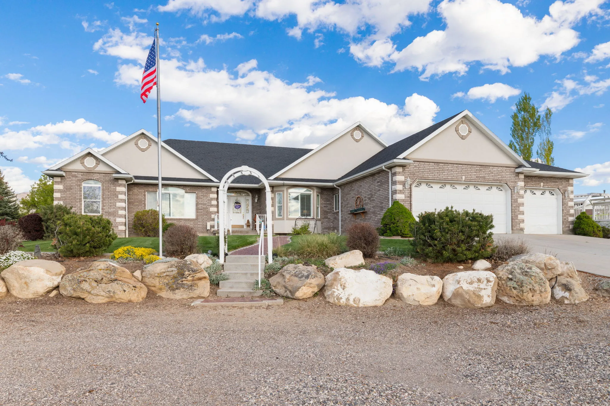 Brick and siding exterior featuring two attached garages, a concrete driveway, and a landscaped front yard with a stone retaining wall