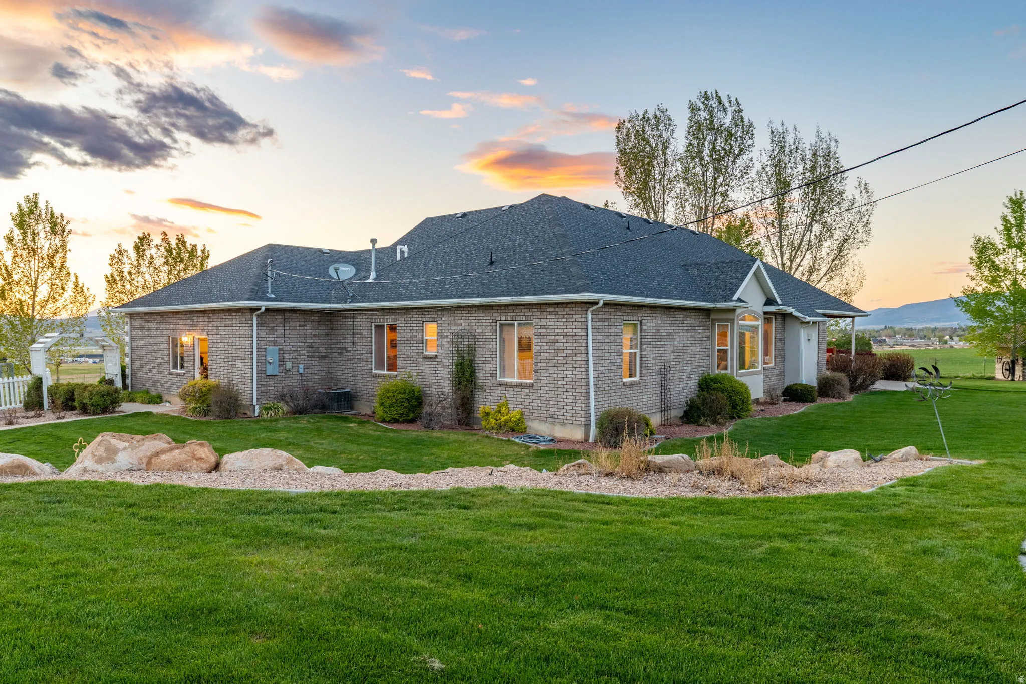 Spacious exterior featuring a brick facade, dark shingle roof, and a meticulously manicured lawn