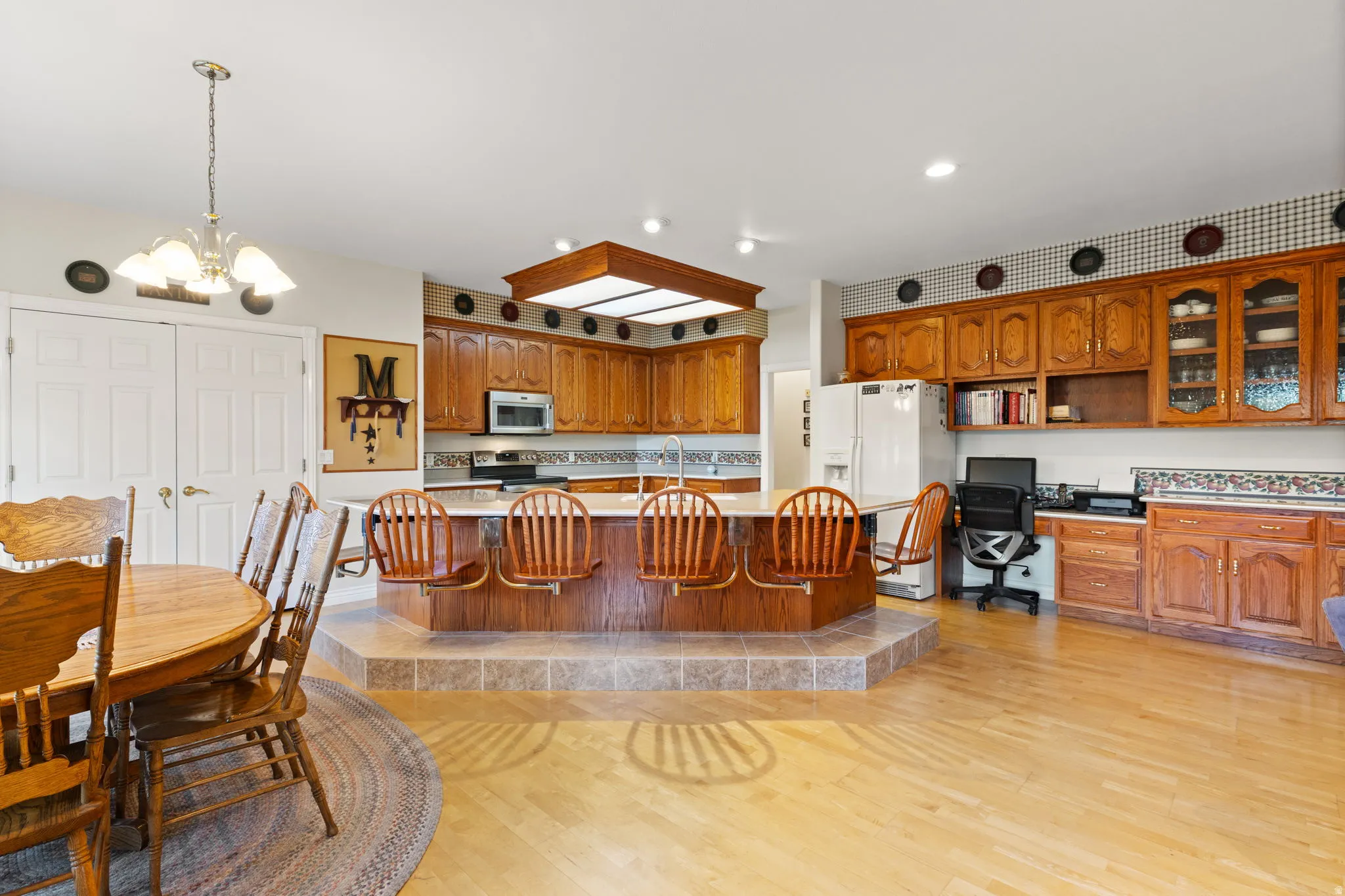 Spacious kitchen featuring a central tiered island with seating, extensive wood cabinetry, and a built-in office nook