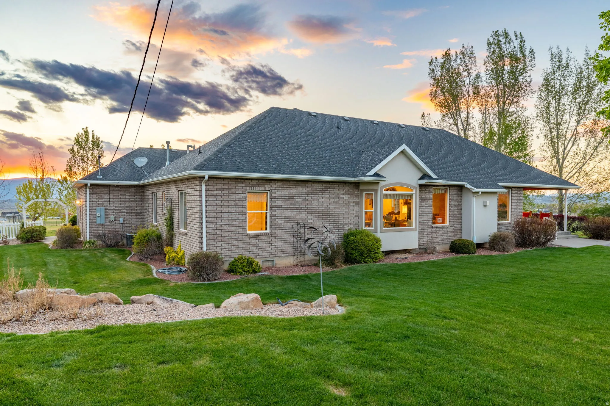 Brick exterior with a dark shingle roof, featuring a bay window, covered patio, and a spacious lawn with established landscaping