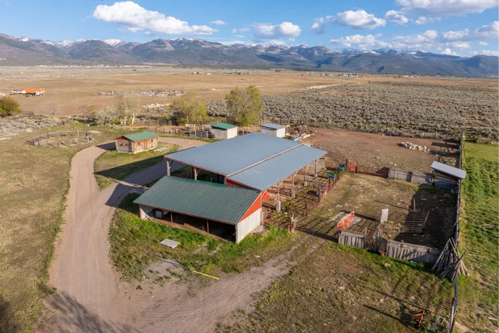 Expansive property featuring a large red barn with a gray metal roof, multiple fenced enclosures, and a dirt driveway