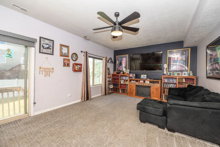 Carpeted living area featuring a ceiling fan with integrated lighting, a sliding glass door providing outdoor access, and a built-in media console with an electric fireplace