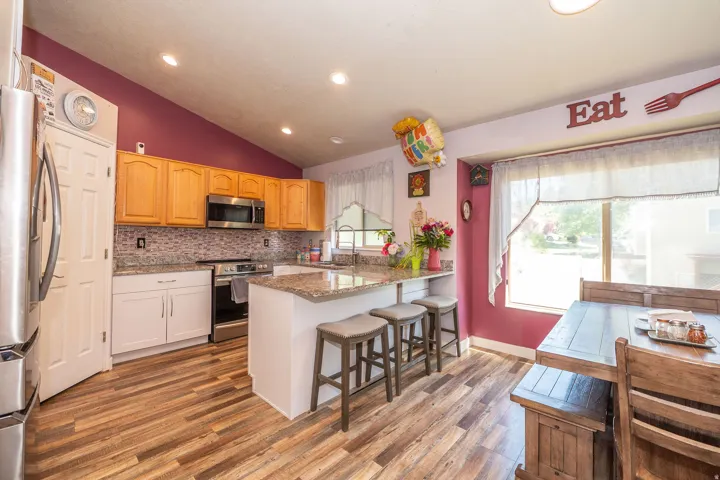 Kitchen featuring wood-finish flooring, a vaulted ceiling, recessed lighting, a stone-finish backsplash, and an island with a stone-finish countertop