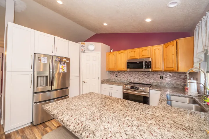Kitchen featuring a central island with a granite-style countertop, stainless steel appliances, wood-finish flooring, recessed lighting, and a mosaic tile backsplash