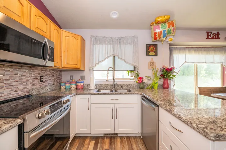 Kitchen featuring stainless steel appliances, wood-finish flooring, white lower cabinetry, natural wood upper cabinetry, and a mosaic tile backsplash