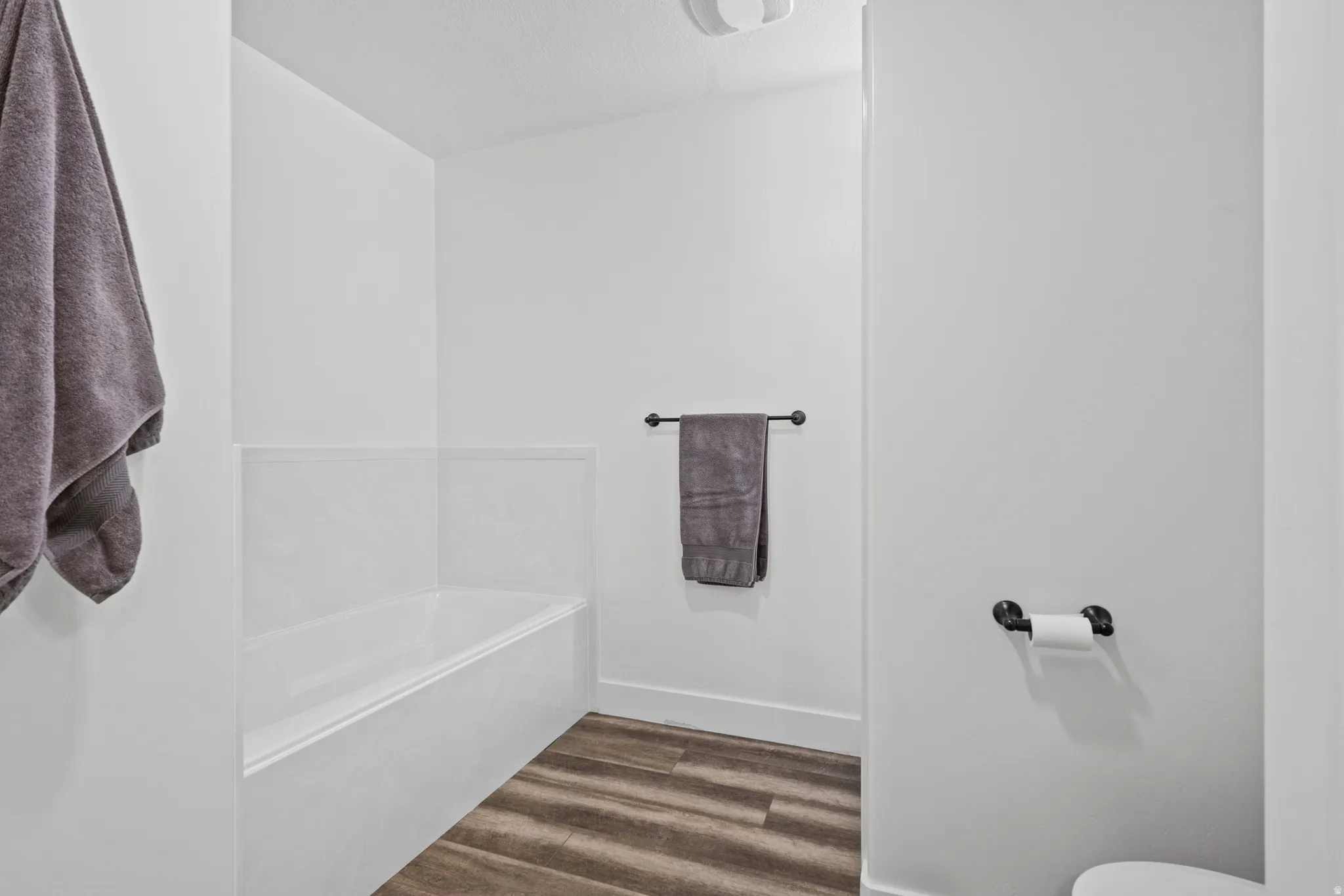White bathtub with a tiled surround, wood-finish flooring, and a towel bar featuring matte black hardware