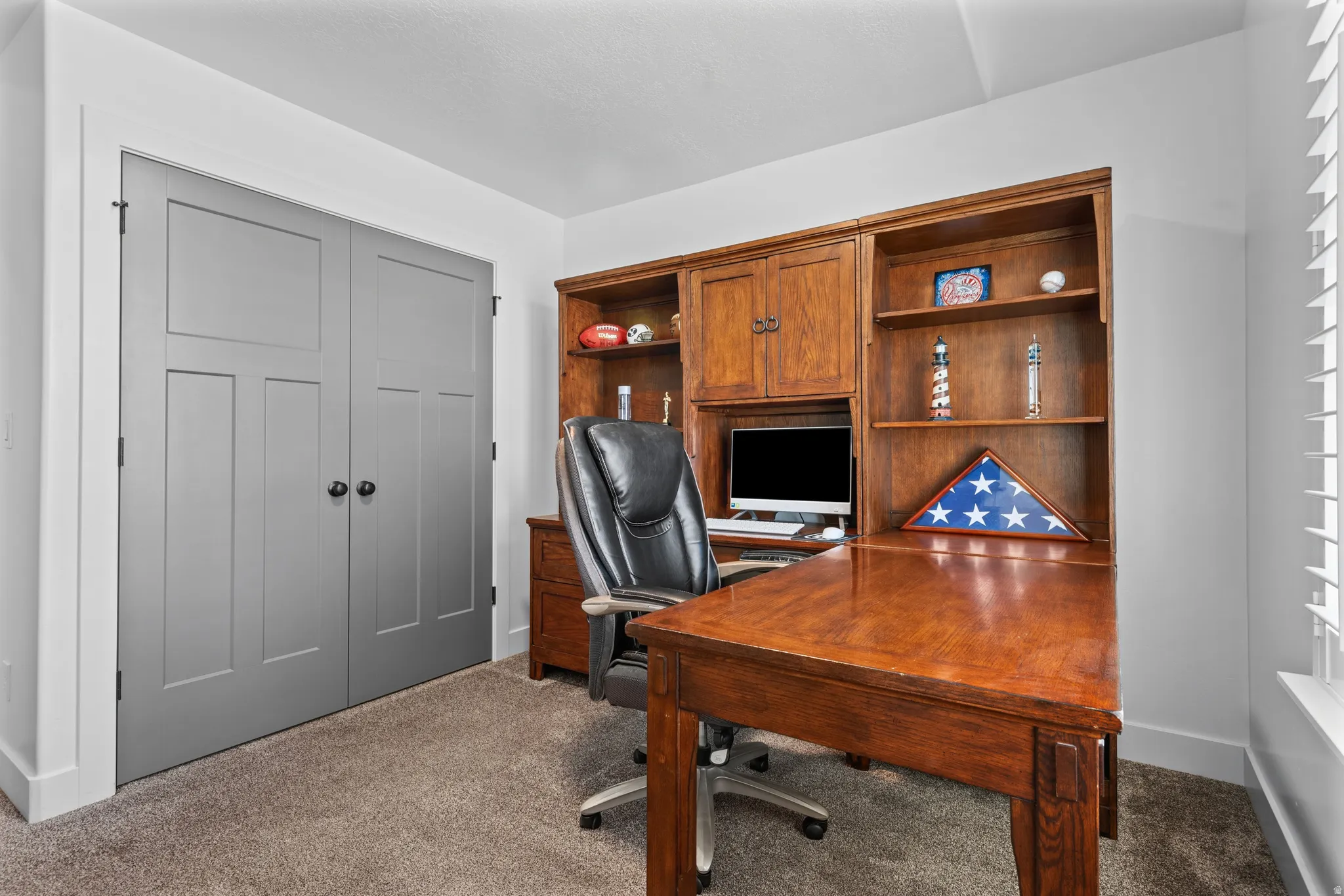 Dedicated space featuring a built-in wood desk and shelving unit, neutral wall color, gray bi-fold doors, white baseboards, and carpet flooring