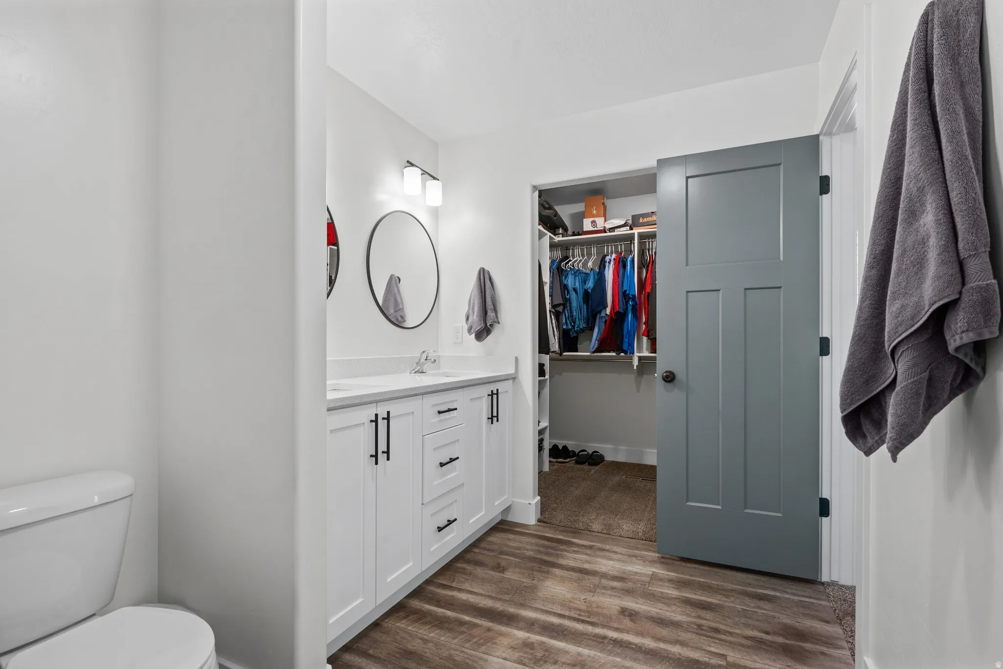 Bathroom vanity featuring dual sinks, white cabinetry with black hardware, and wood-finish flooring