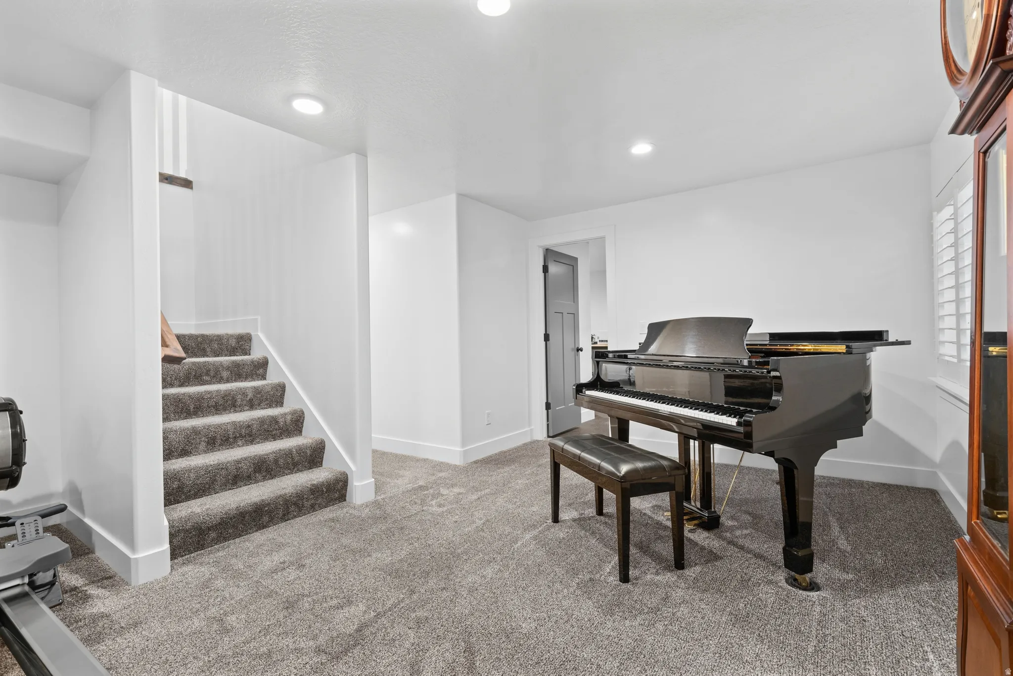 Open-concept lower level featuring plush carpet, recessed lighting, white trim work, and a private staircase with carpeted treads
