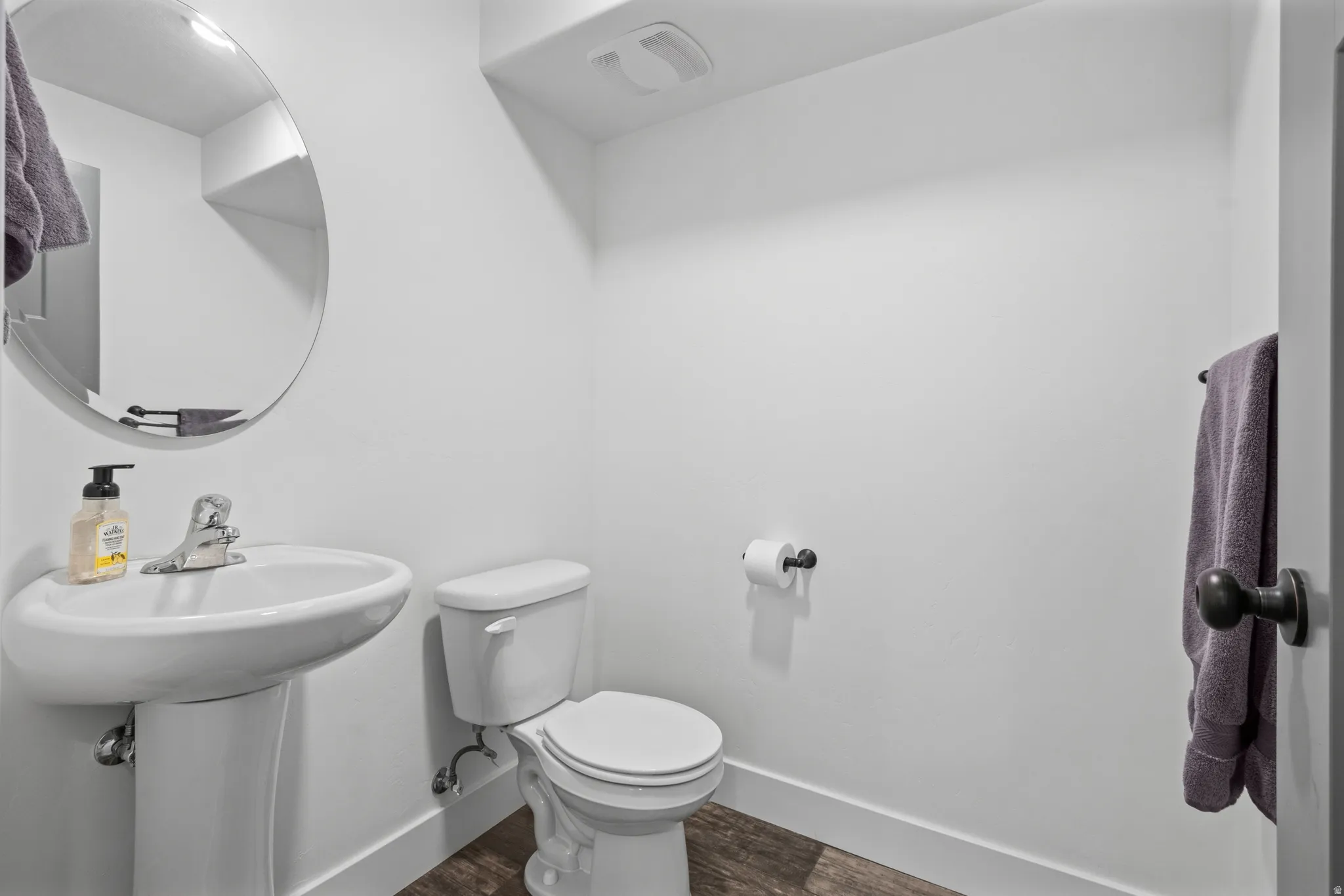 Pedestal sink with chrome faucet, circular mirror, and dark wood-finish flooring