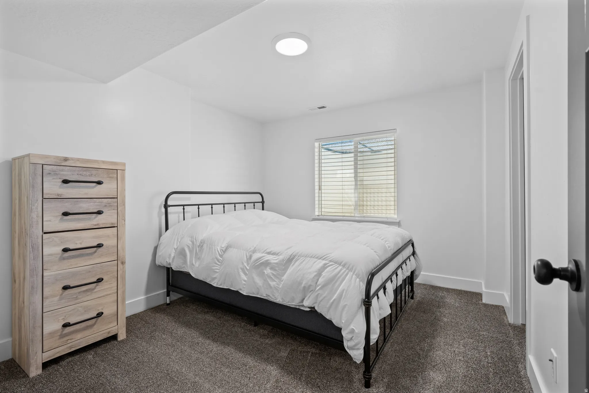 Spacious room featuring neutral carpeting, white walls, and a window with blinds