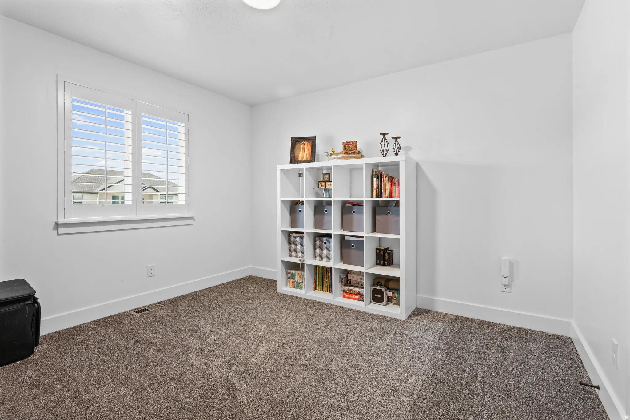 Bright room featuring neutral carpeting, white walls, and a large window with plantation shutters