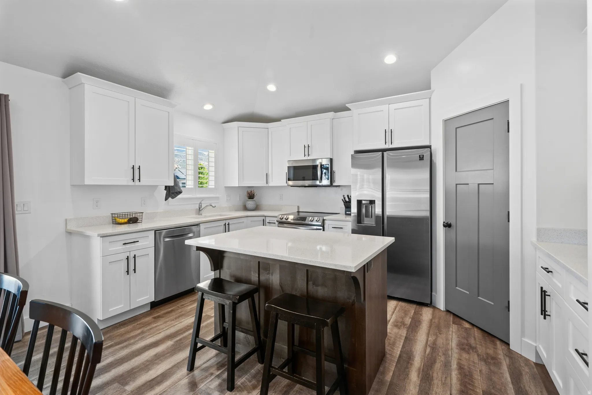Kitchen featuring white cabinetry, stainless steel appliances, a center island with countertop seating, wood-finish flooring, and recessed lighting