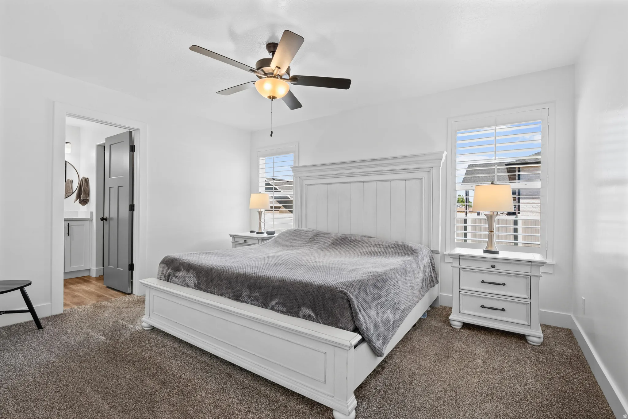 Spacious bedroom featuring neutral carpeting, white trim, a ceiling fan with integrated lighting, and white plantation shutters on the window