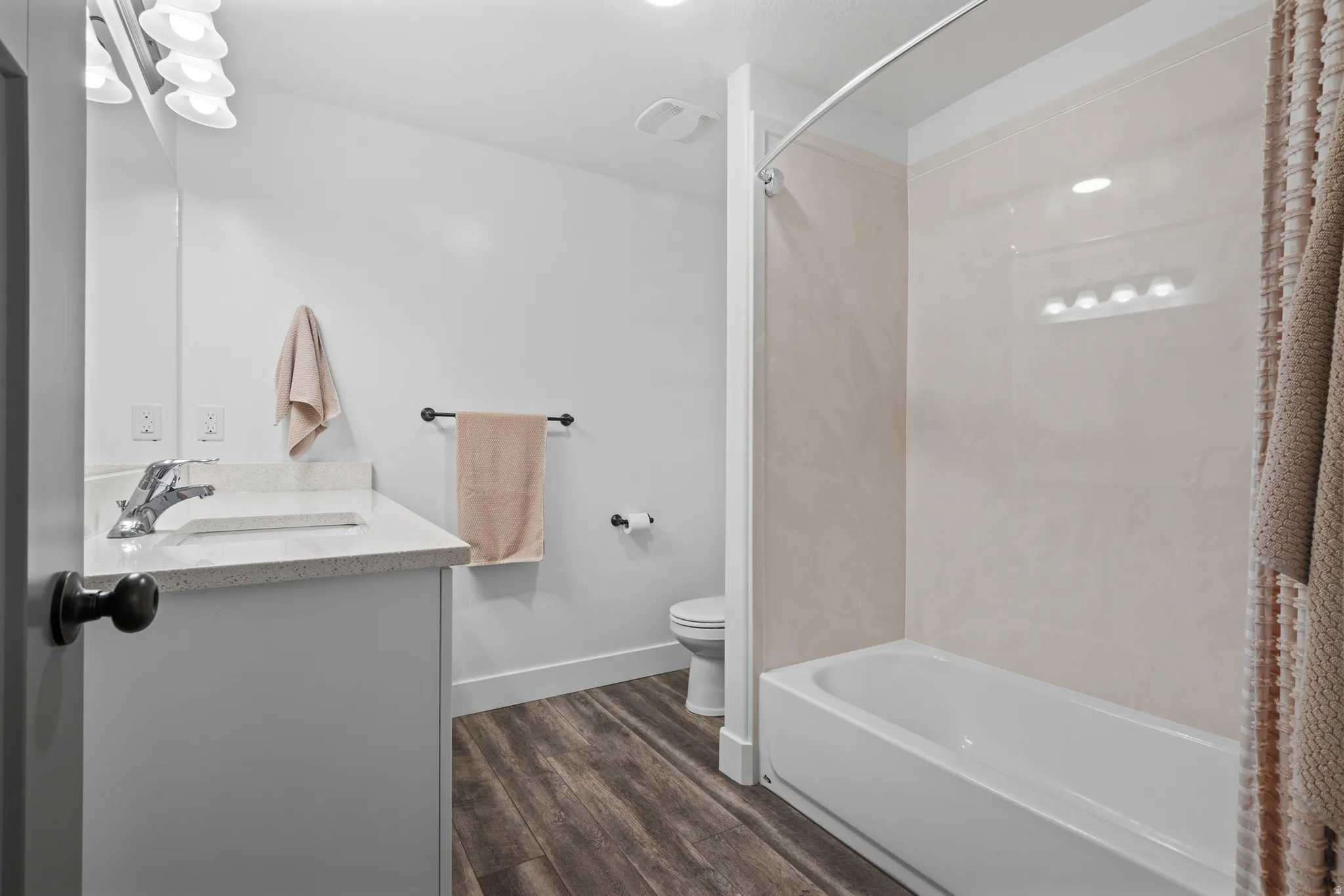 Bathroom with wood-finish flooring, a white vanity with a light-colored countertop, and a white bathtub with a beige wall surround