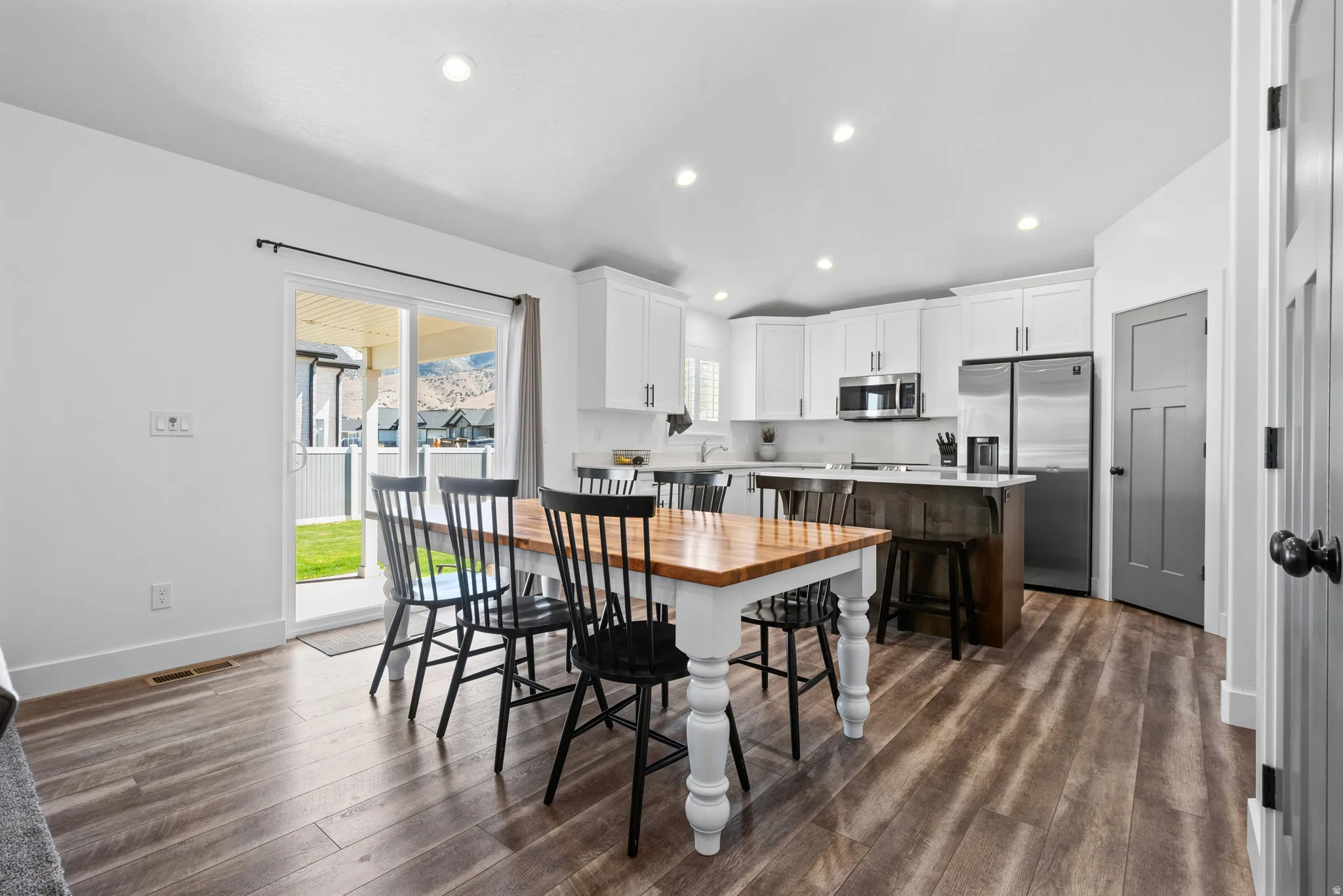 Open-concept kitchen and dining area featuring wood-finish flooring, white cabinetry, recessed lighting, and stainless steel appliances