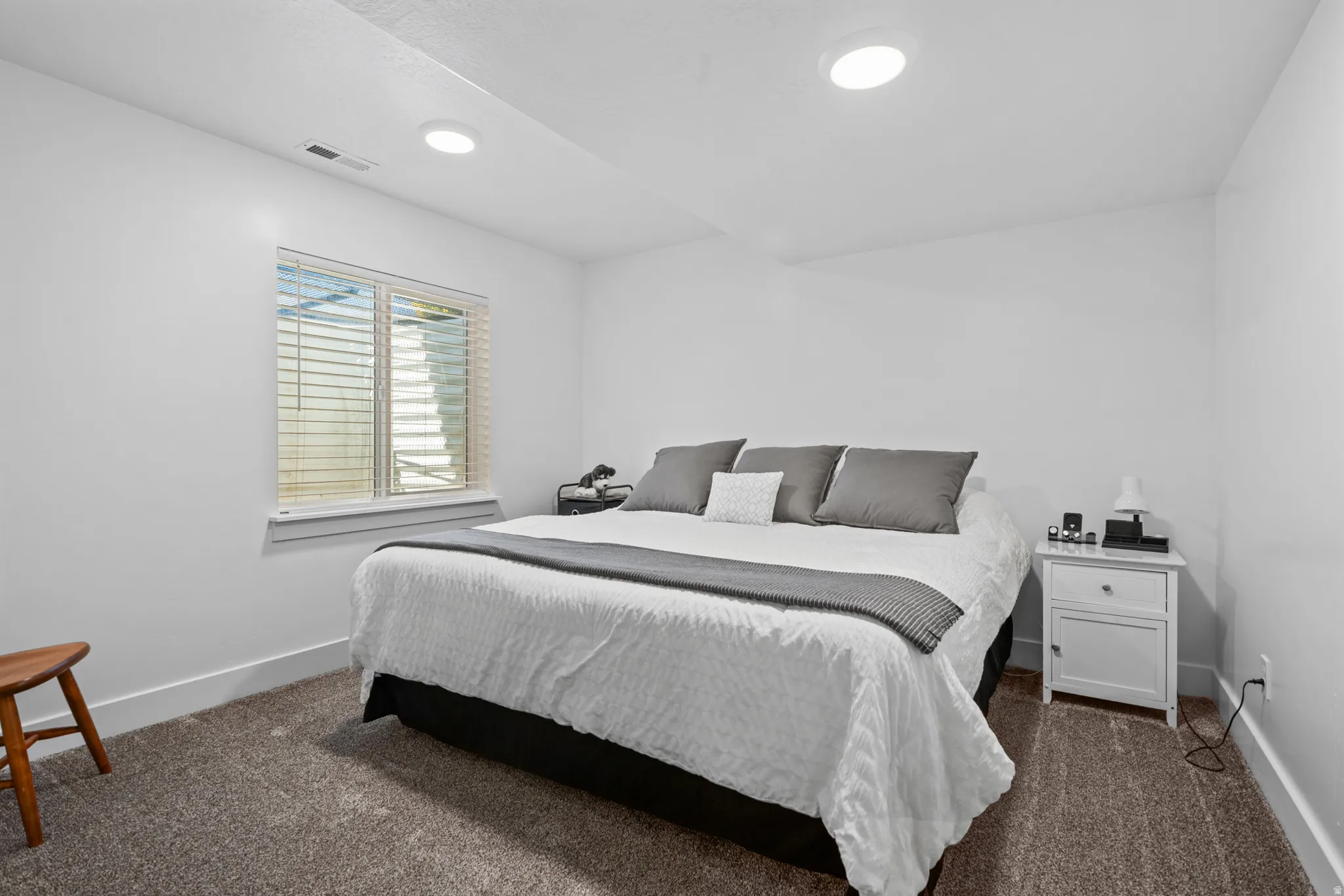Bedroom featuring plush carpet flooring, recessed ceiling lighting, a white window frame with blinds, and white baseboards