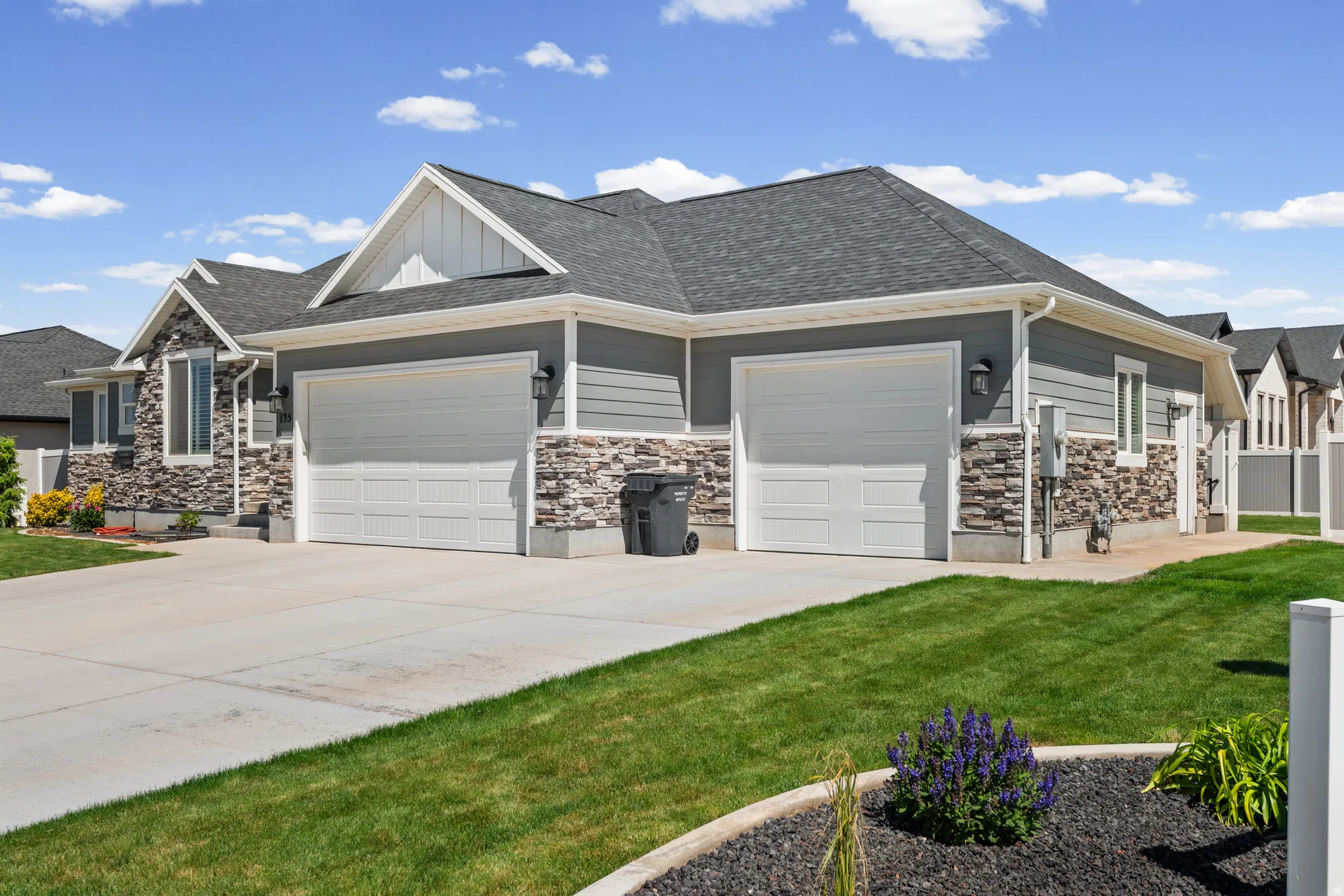Contemporary ranch-style residence featuring a two-car garage, gray horizontal siding, and stone accents