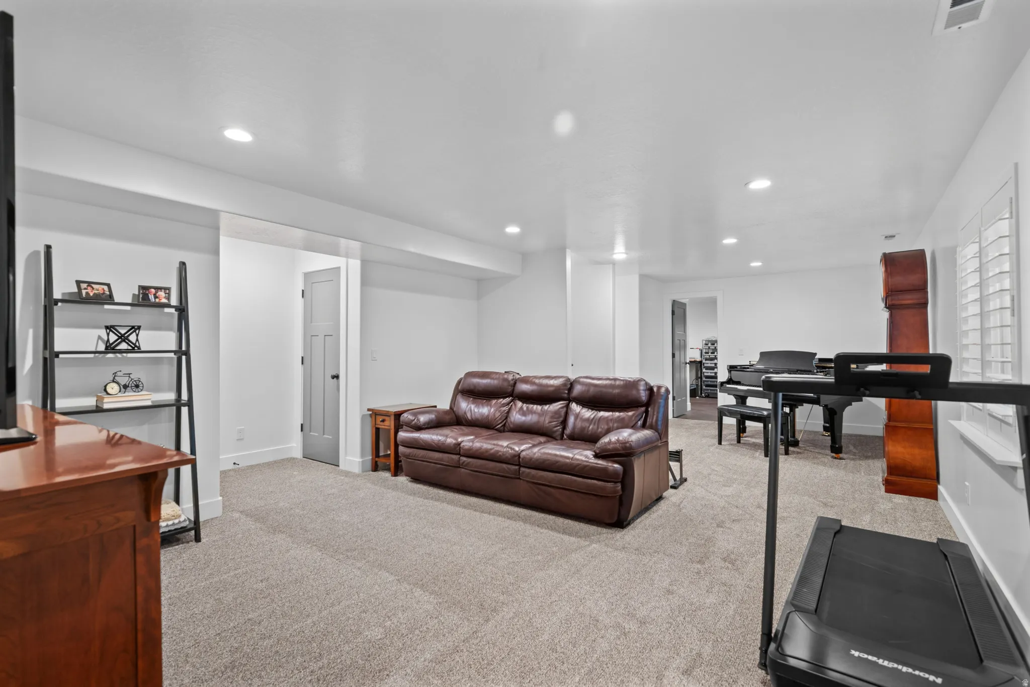 Spacious carpeted room featuring white walls, recessed lighting, and white window shutters