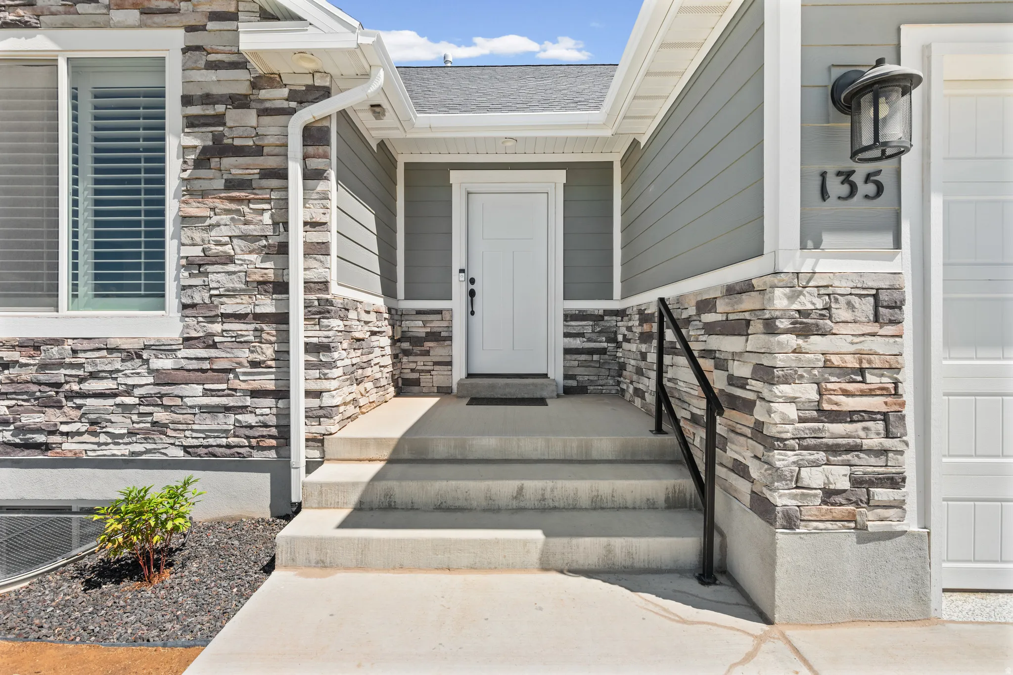 Stone veneer and siding exterior featuring a multi-level concrete entry, dark house numbers, an exterior lantern light fixture, and a white entry door