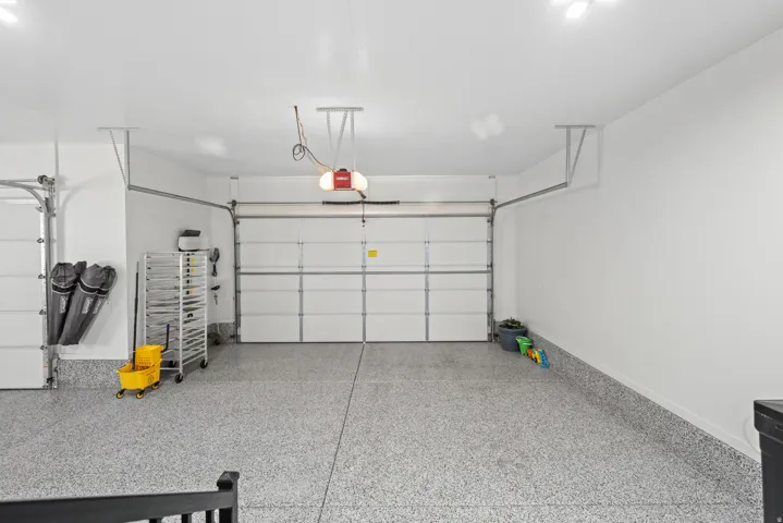 Three-car garage featuring an epoxy floor finish, two overhead garage doors with automatic openers, and recessed lighting