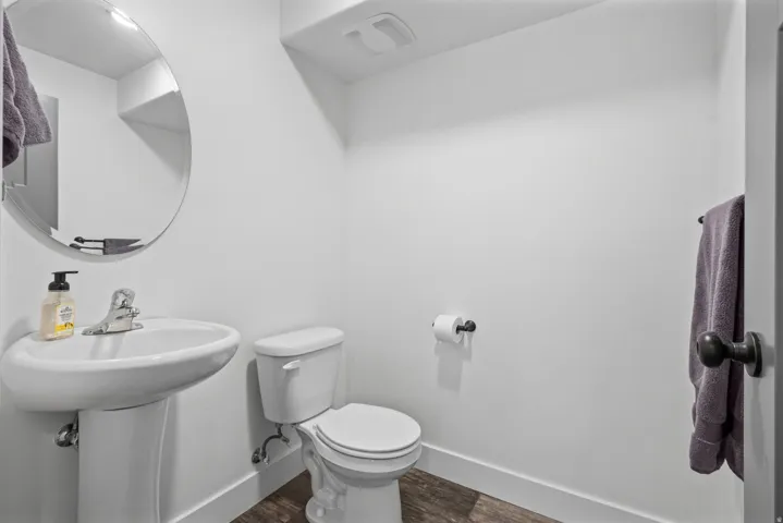 Pedestal sink with chrome faucet, circular mirror, and dark wood-finish flooring