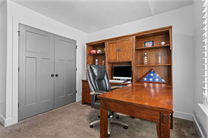 Dedicated space featuring a built-in wood desk and shelving unit, neutral wall color, gray bi-fold doors, white baseboards, and carpet flooring