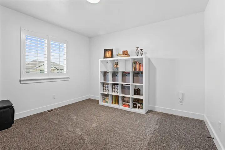 Bright room featuring neutral carpeting, white walls, and a large window with plantation shutters