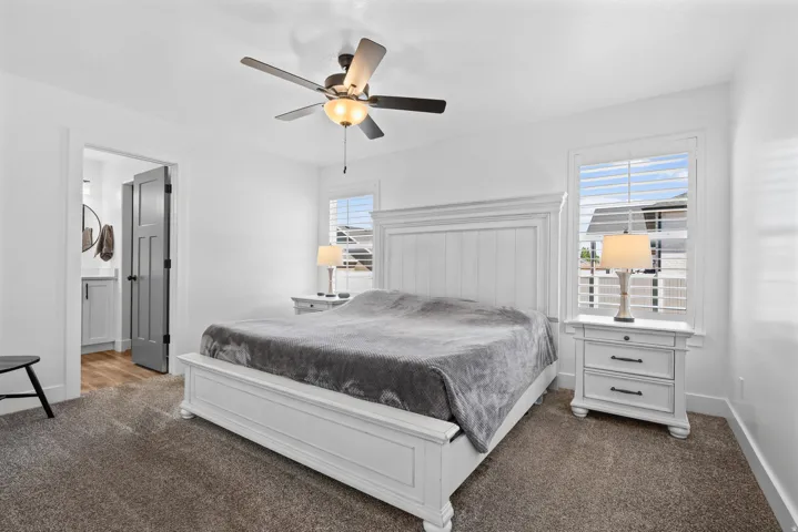 Spacious bedroom featuring neutral carpeting, white trim, a ceiling fan with integrated lighting, and white plantation shutters on the window