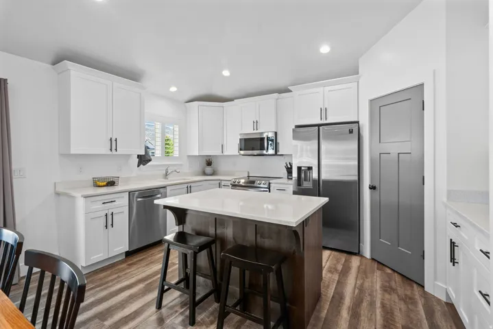 Kitchen featuring white cabinetry, stainless steel appliances, a center island with countertop seating, wood-finish flooring, and recessed lighting
