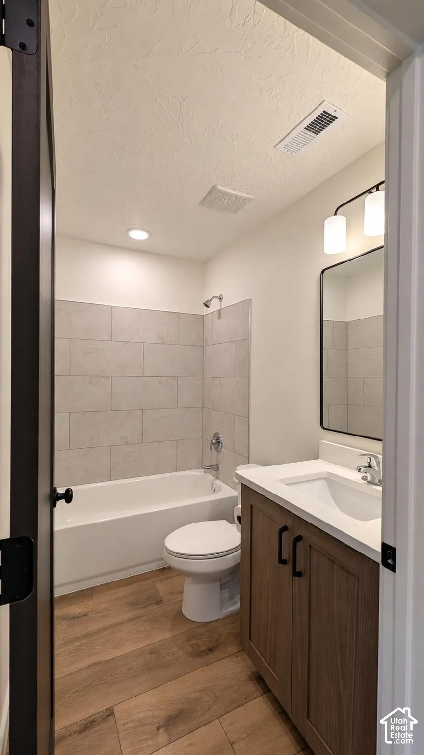 Wood-finish flooring, full bathtub with tile surround, single vanity with white countertop, and contemporary wall-mounted lighting