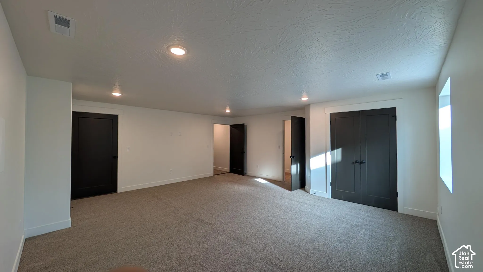 Spacious room with gray carpeting, recessed ceiling lighting, white walls, and dark interior doors