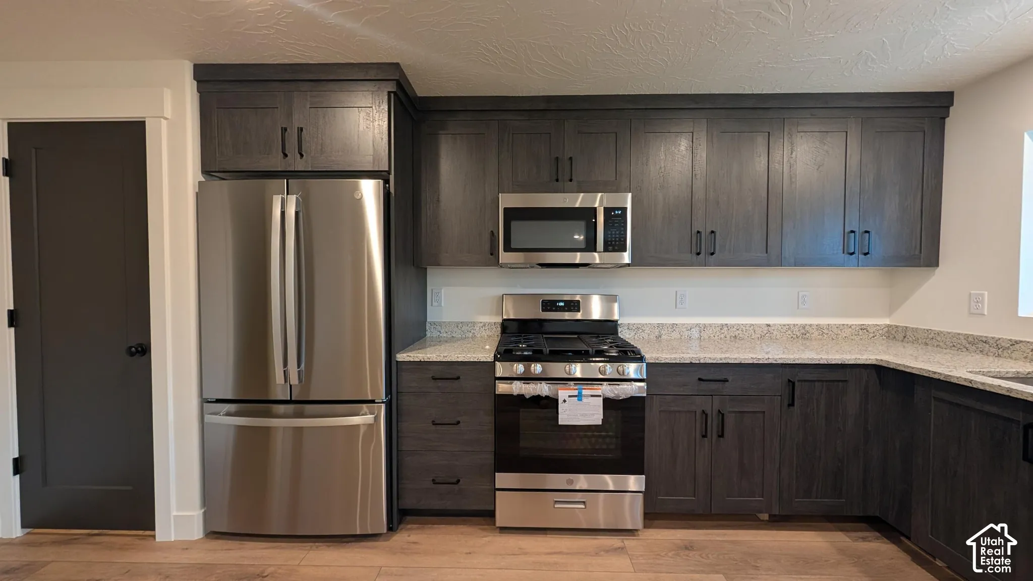 Stainless steel refrigerator, stainless steel gas range, stainless steel microwave, dark wood-finish cabinetry, and light-colored countertops