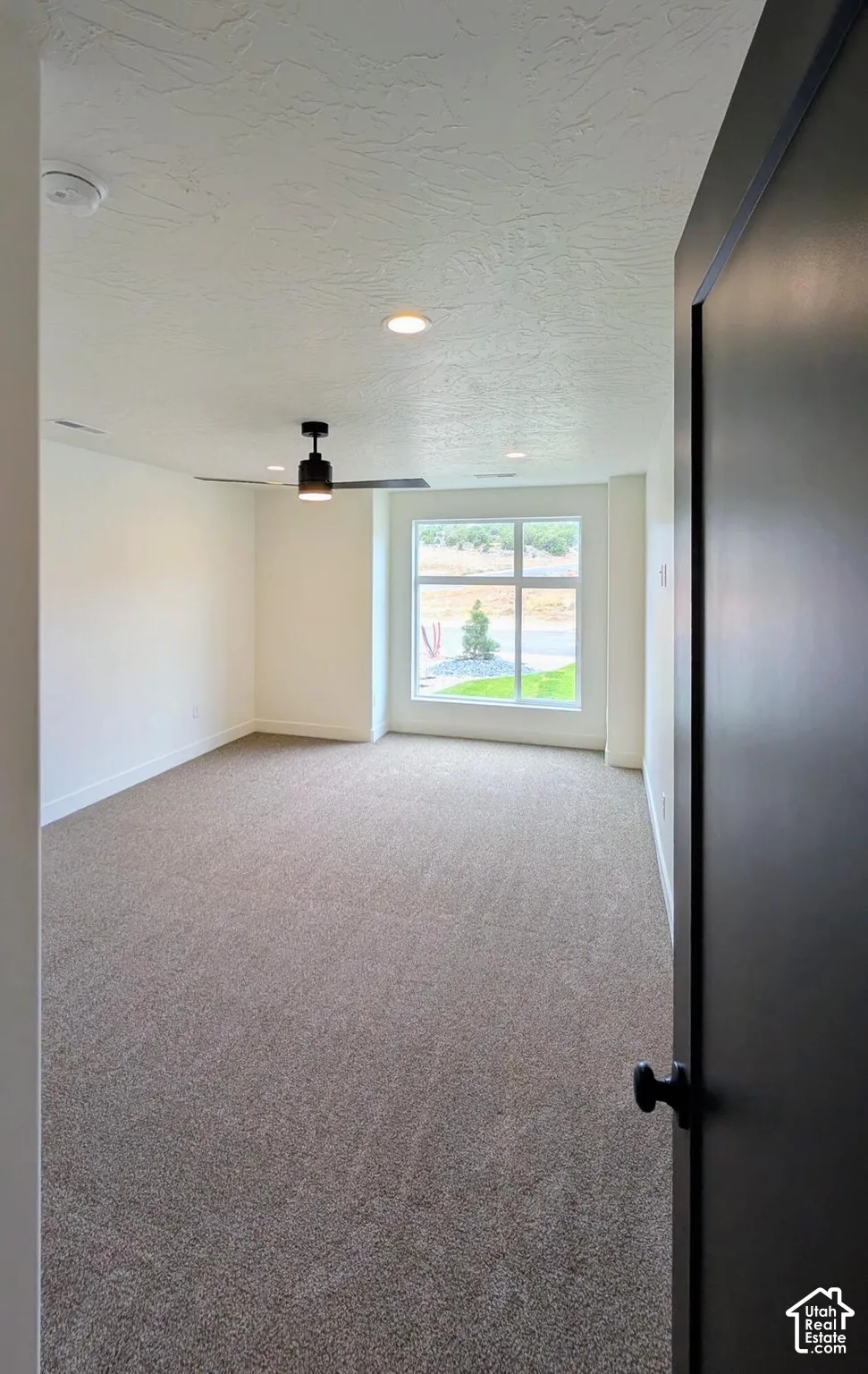 Spacious room featuring neutral carpeting, a large window, a modern ceiling fan, and recessed lighting