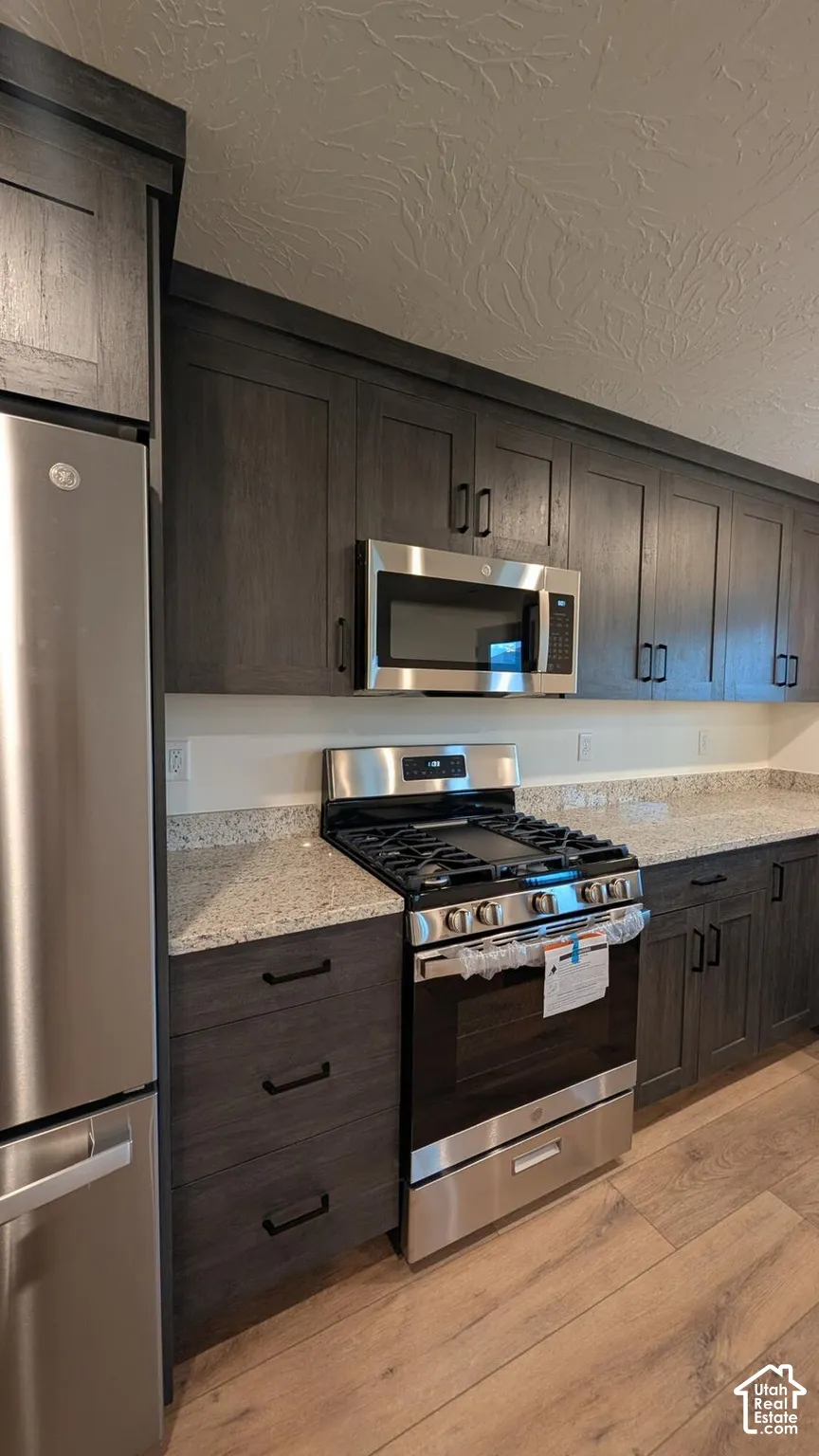 Stainless steel appliances, wood-finish flooring, dark wood cabinetry, light-toned countertops, and an integrated microwave