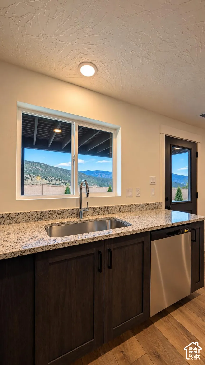 Stainless steel sink with a gooseneck faucet, light-toned countertop, wood-finish cabinetry, built-in dishwasher, and wood-finish flooring