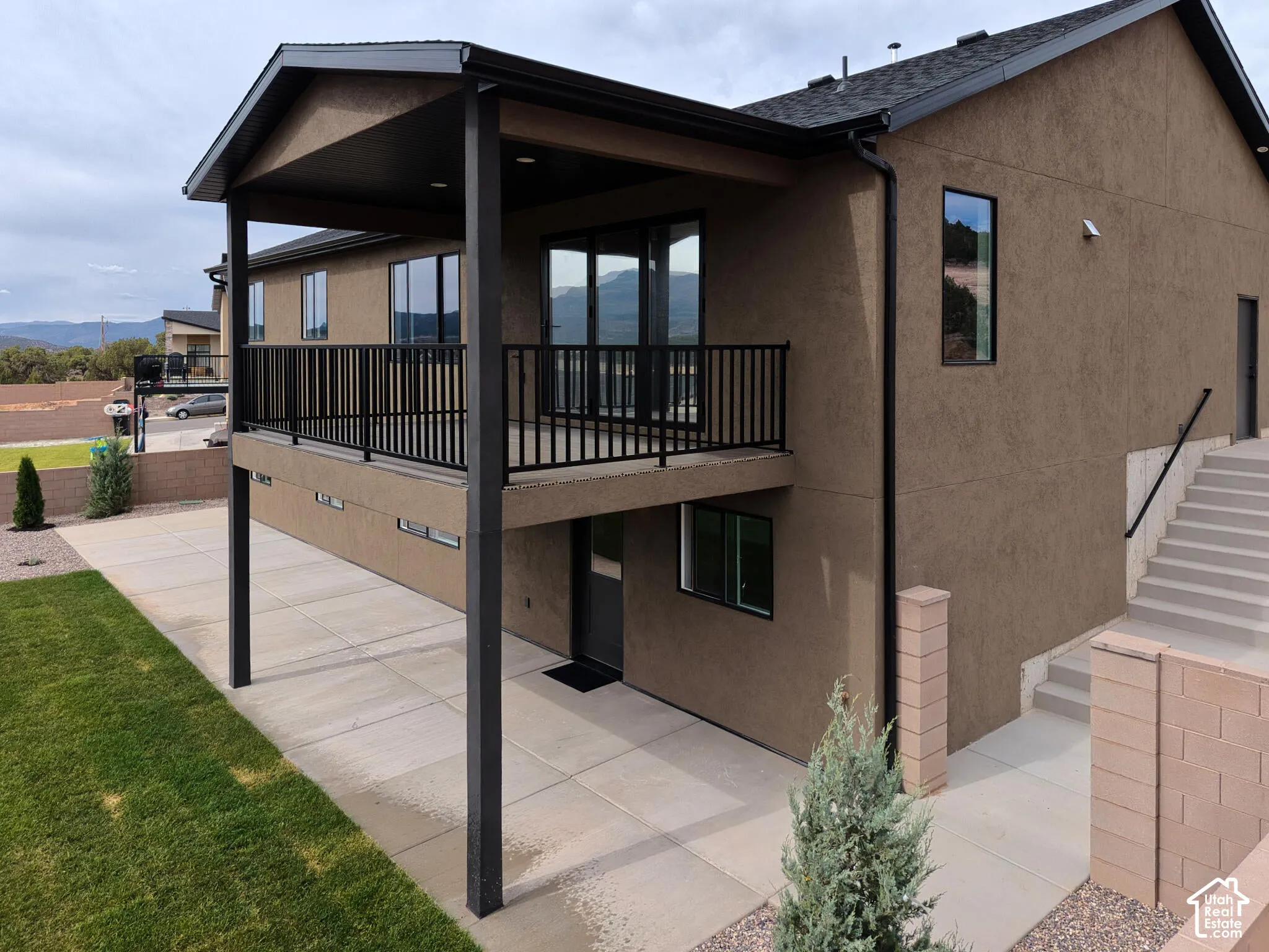 Stucco exterior featuring a covered deck with black railing, multiple windows, and exterior stairs