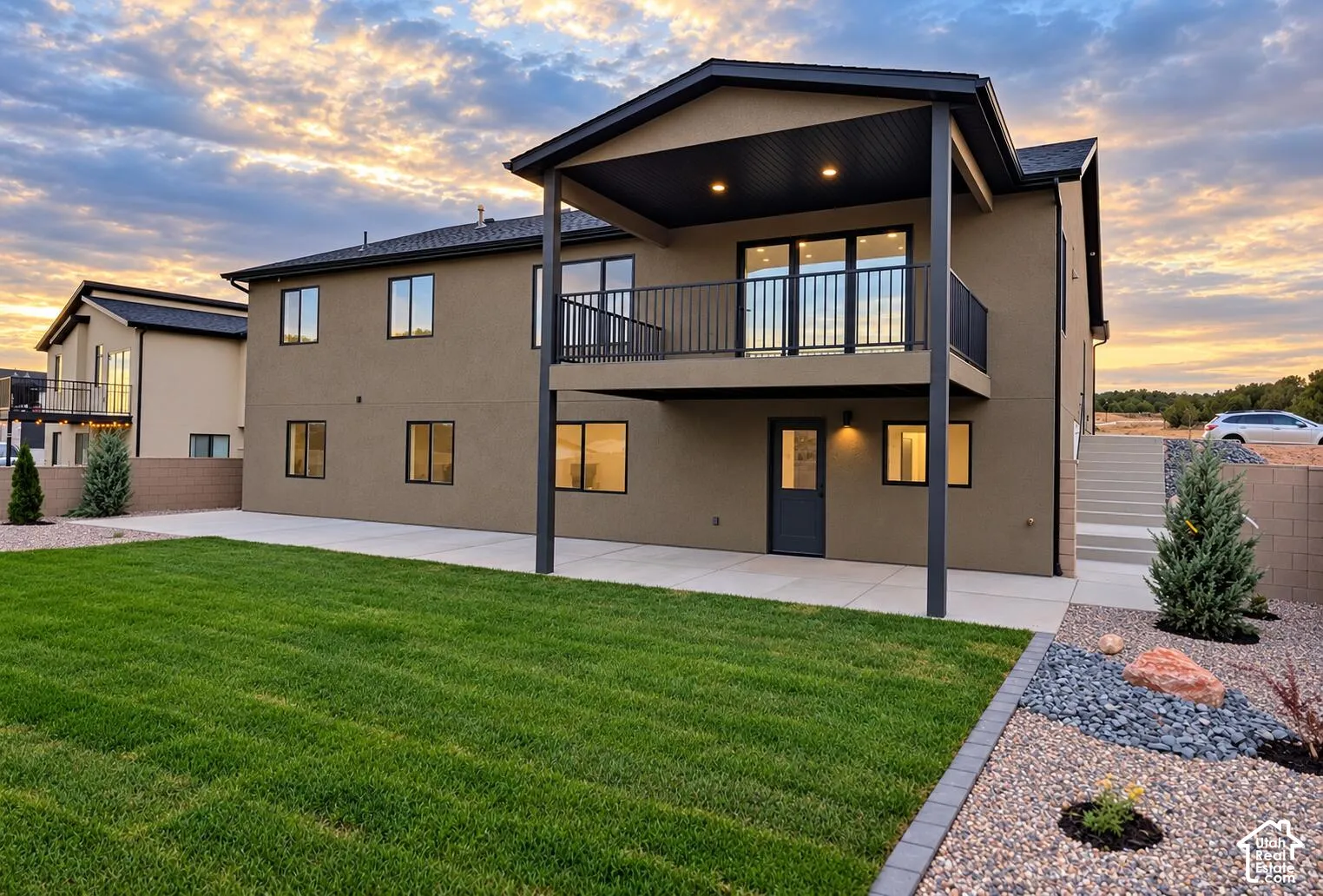 Multilevel exterior with a covered balcony, lower-level patio, and an expansive lawn area