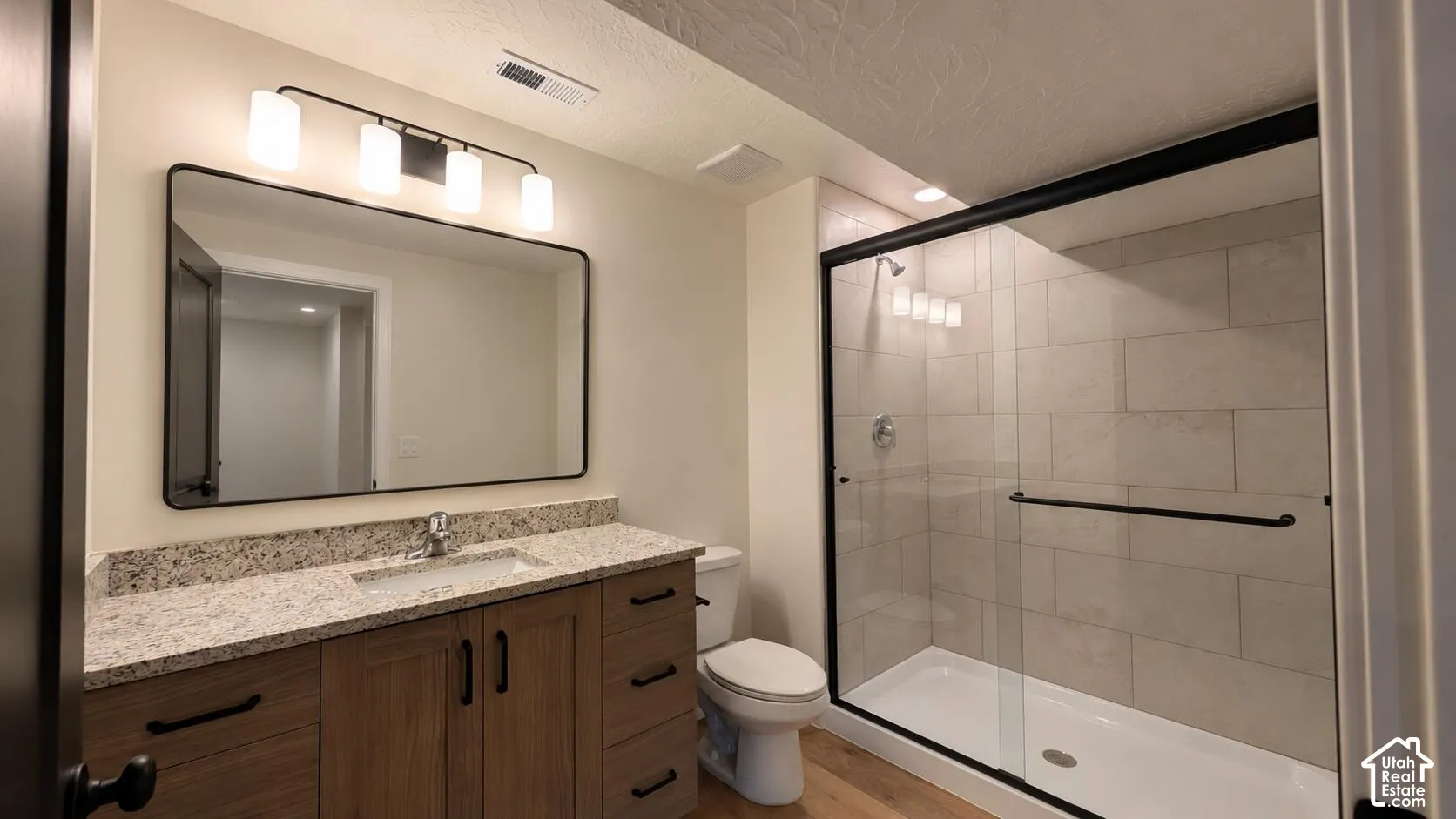 Bathroom featuring a wood-tone vanity with a light-toned countertop, rectangular mirror, and a walk-in shower with a glass enclosure