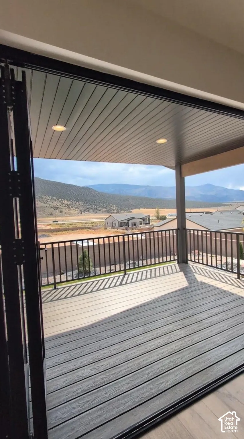 Sliding glass panel doors open to an expansive covered deck with composite decking and black metal railings, featuring recessed lighting and distant mountain scenery