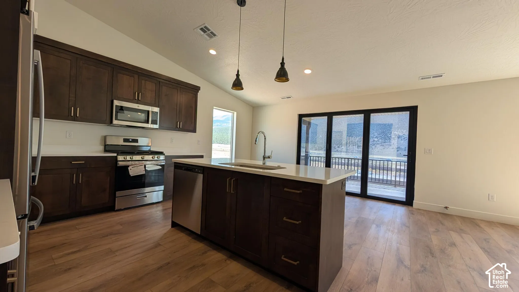 Open-concept living space with a vaulted ceiling, wood-finish flooring, and a kitchen island featuring a sink and pendant lighting