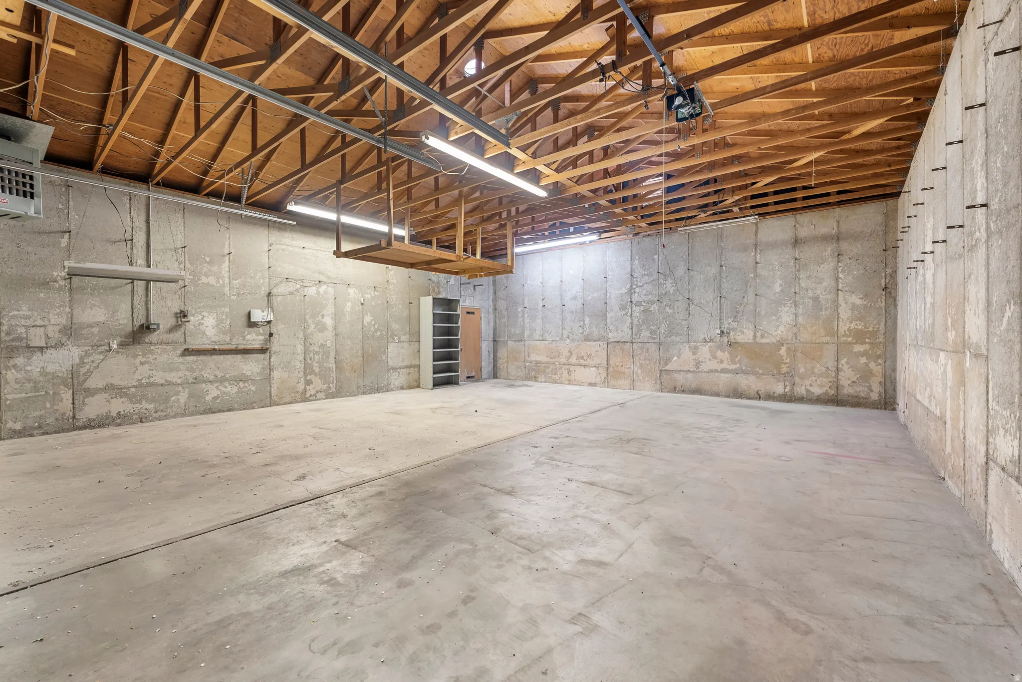 Spacious unfinished basement featuring exposed wood ceiling joists, concrete flooring, and bare concrete walls