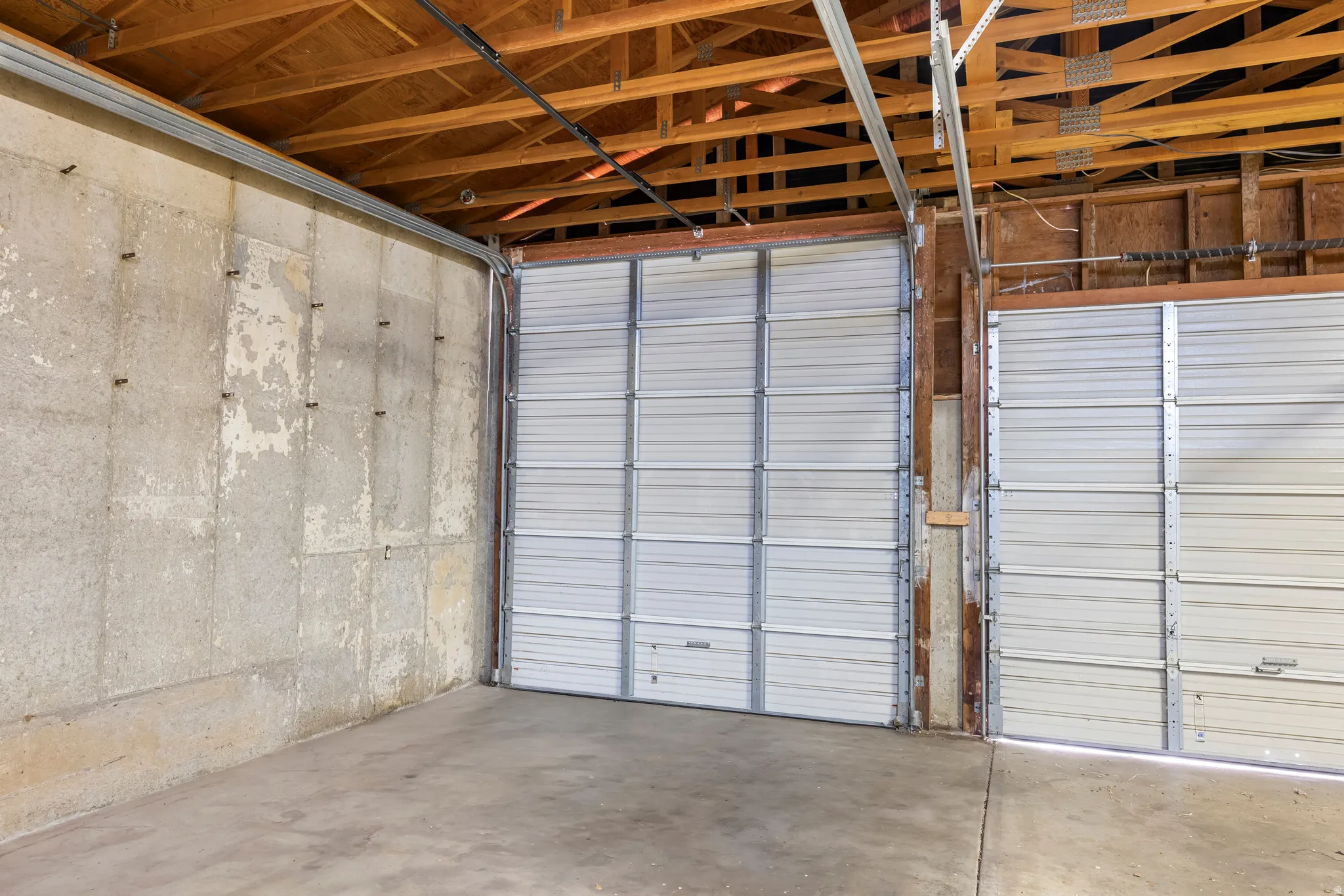 Interior featuring exposed wood beams, concrete flooring, and two roll-up garage doors