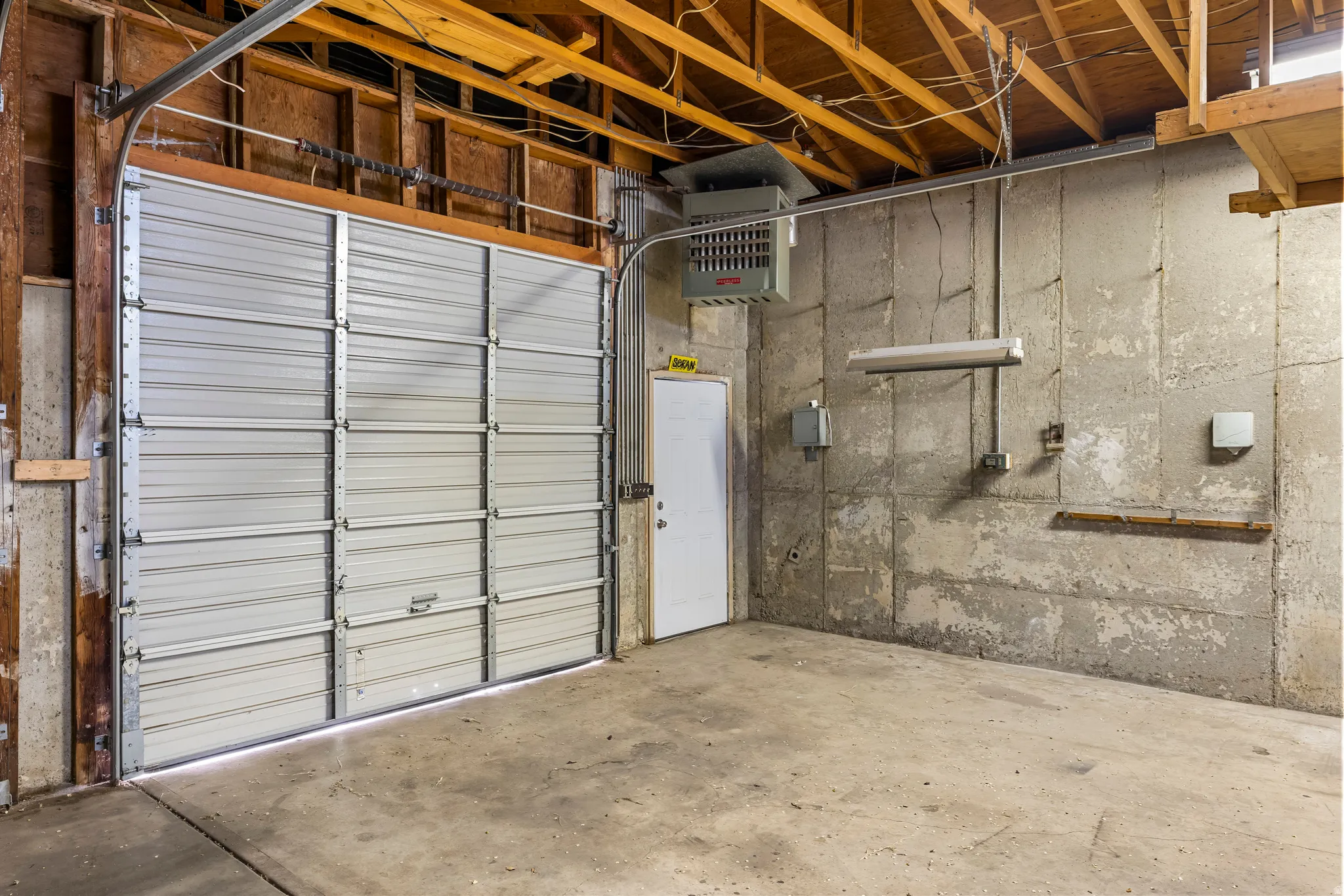 Spacious utility area featuring a large overhead door, concrete flooring, exposed wood beam ceiling, and an entry door