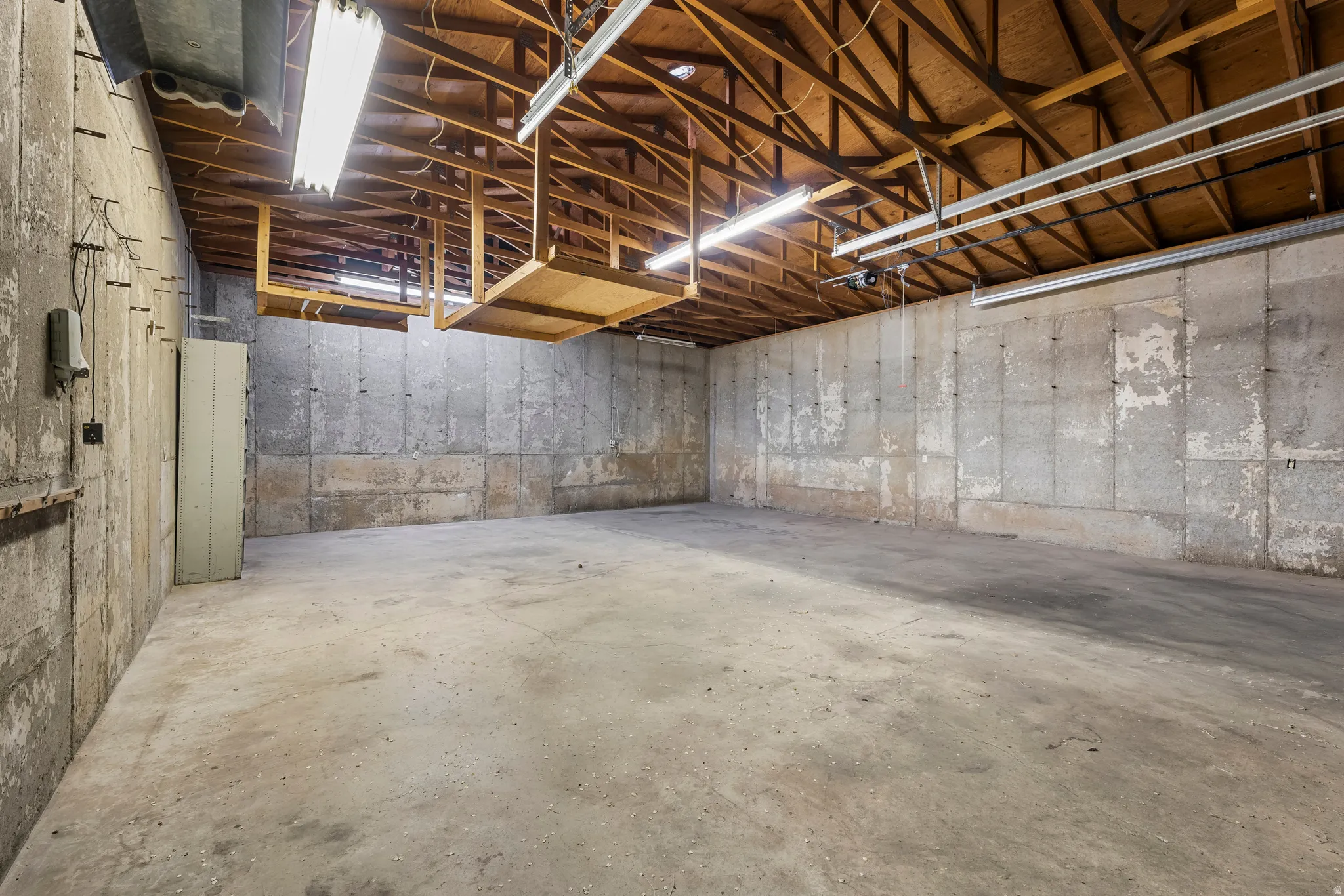 Expansive concrete floor space with exposed wood beam ceiling, concrete block walls, fluorescent lighting, and visible utility conduit