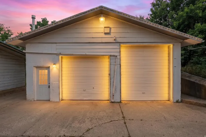 Detached garage featuring two overhead doors, a pedestrian entrance with a paneled door and window lites, and exterior wall sconce lighting