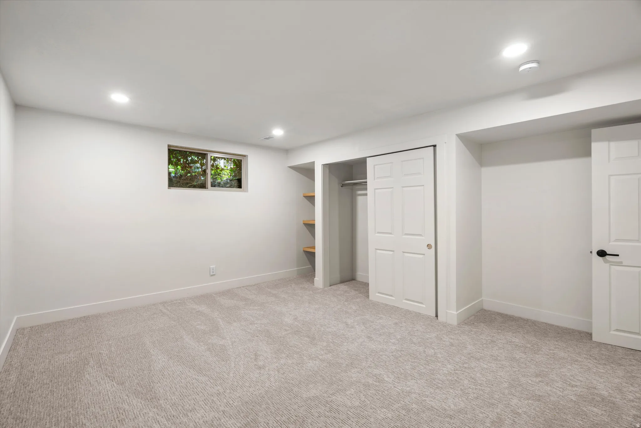Carpeted room featuring recessed lighting, a window with outdoor greenery, bi-fold closet doors, and built-in shelving