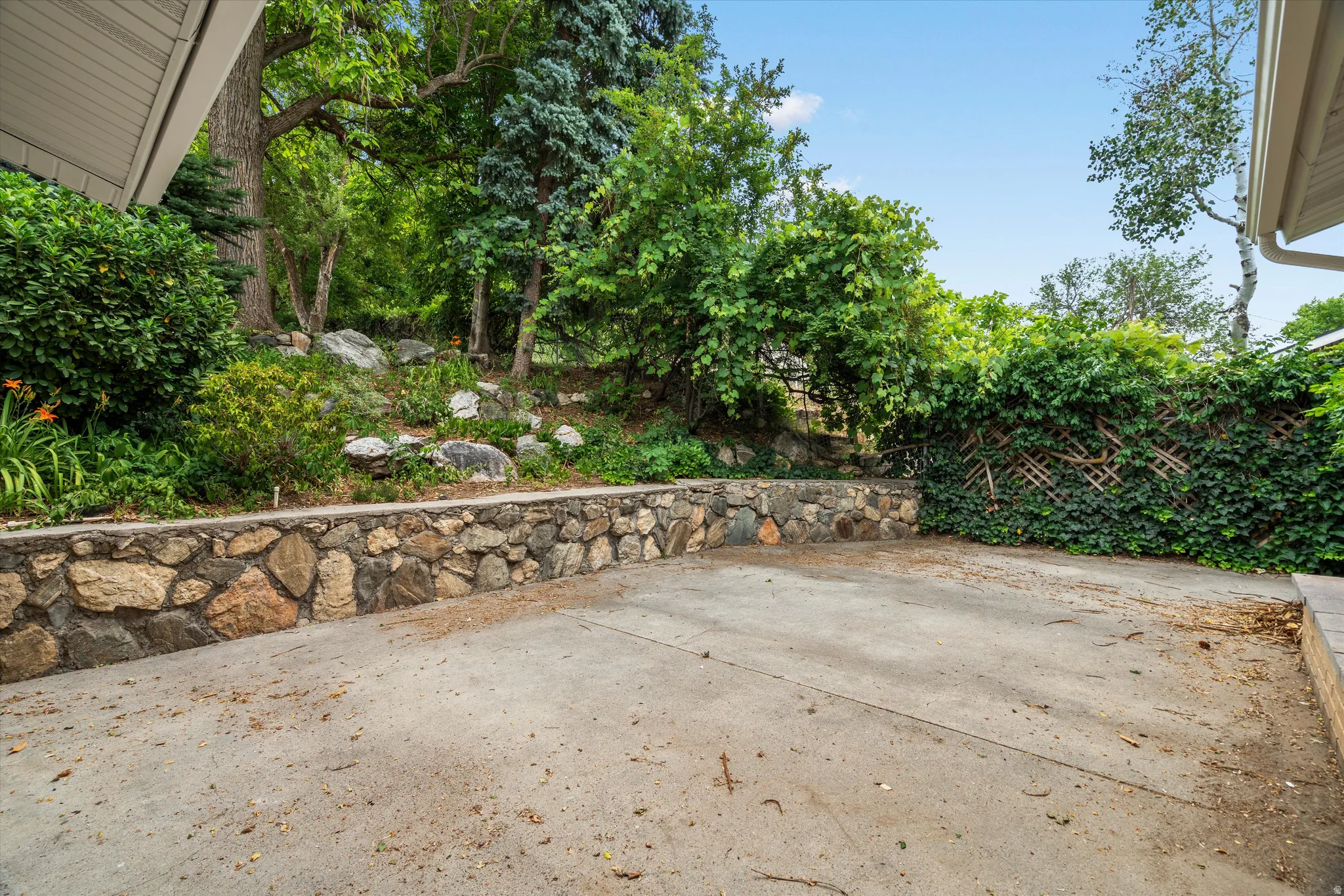 Expansive concrete patio with a stone retaining wall and lush green landscaping