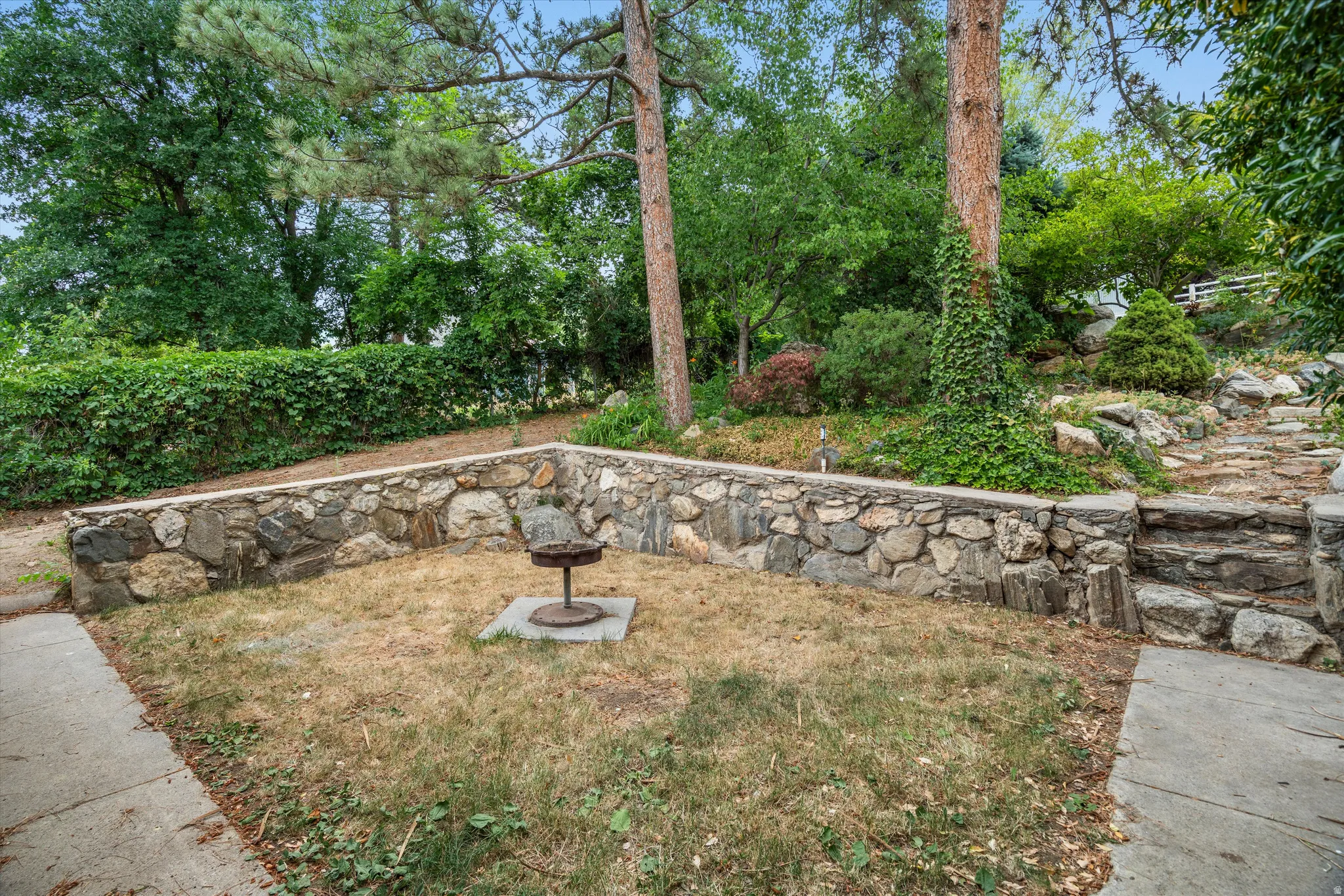 Terraced outdoor area featuring natural stone retaining walls, an integrated built-in grill, and mature trees